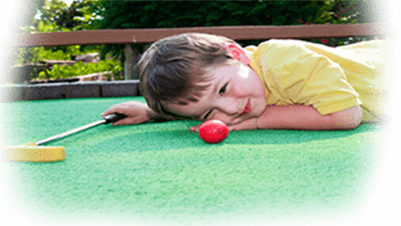 Young boy eyeballing the ball shot at miniature golf